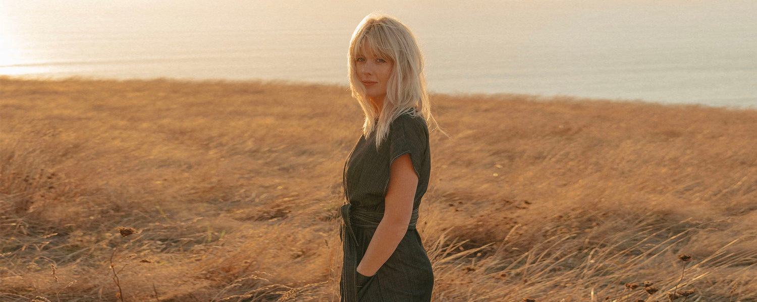 Woman standing in a field near the ocean wearing a dark coloured denim dress